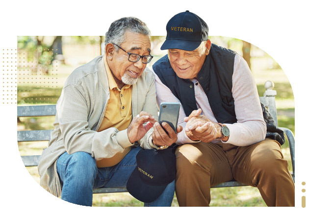 Senior military veterans looking at smartphone social media and talk on bench