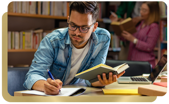 Male student in library writing out research materials