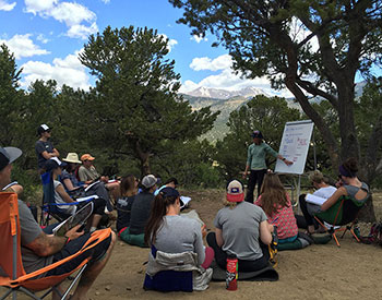 Ski patrol students sit on the ground and in chairs watching the lecturer